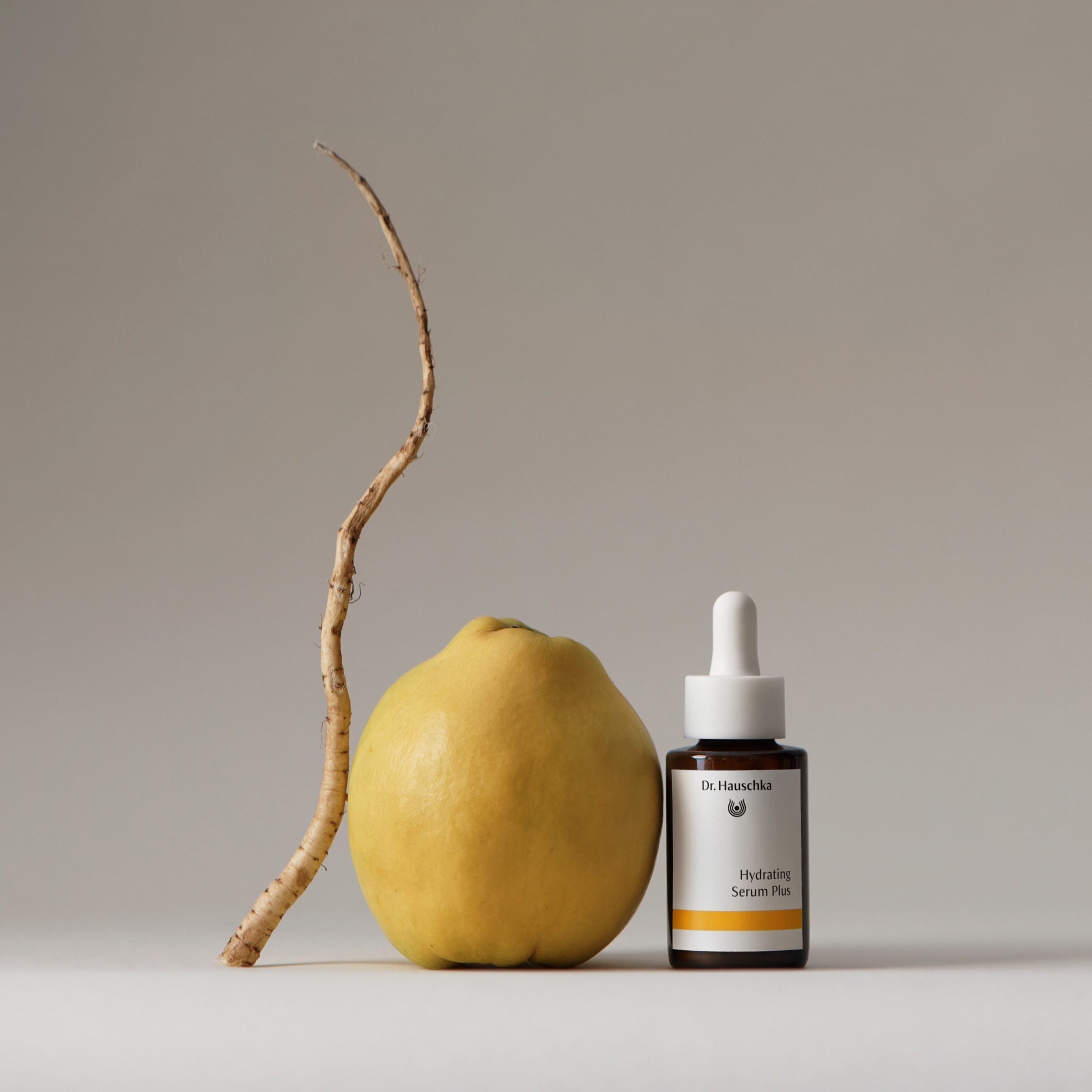 Hydrating Serum Plus von Dr. Hauschka Naturkosmetik, Glasflasche mit Pipette neben einer Quitte